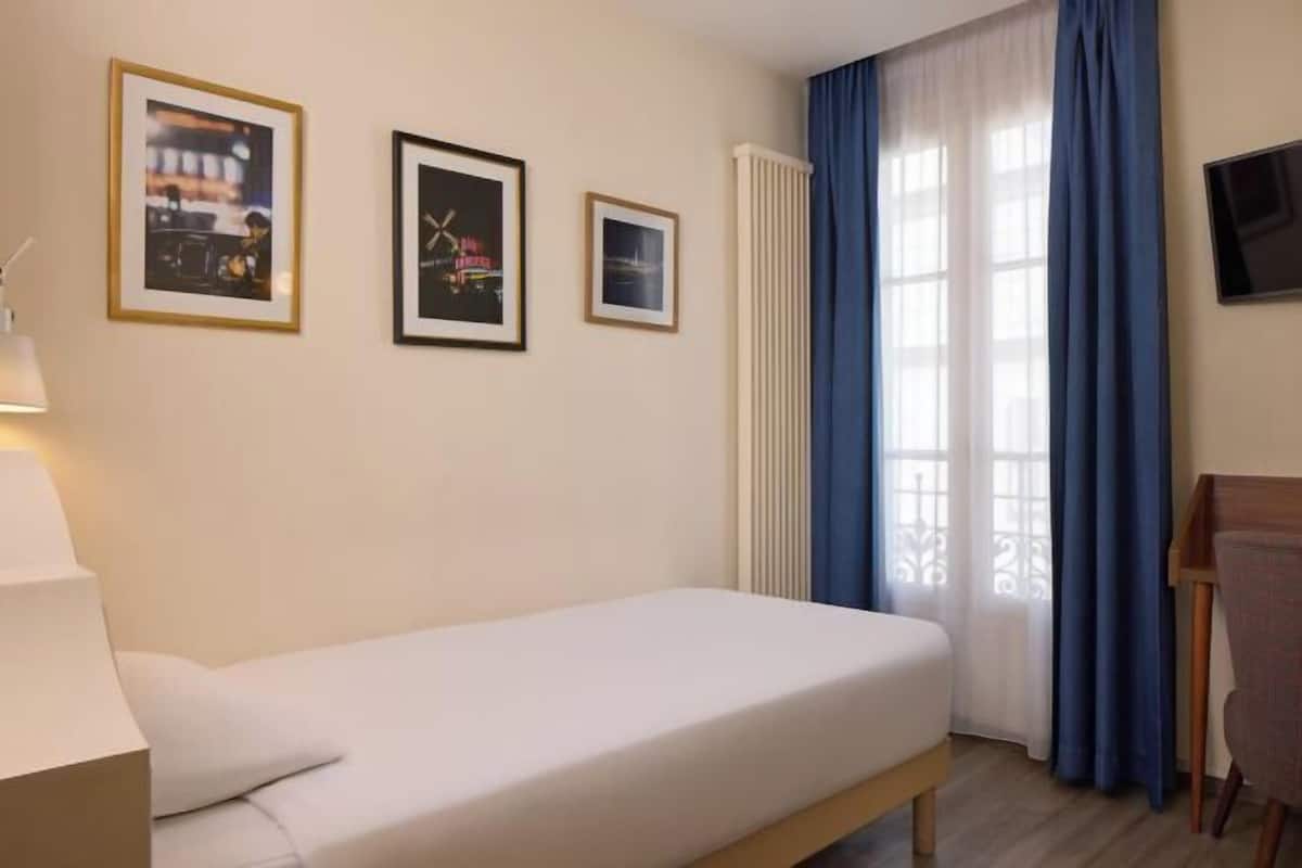 Una cama individual en una habitación con un escritorio, una silla y tres cuadros en la pared.