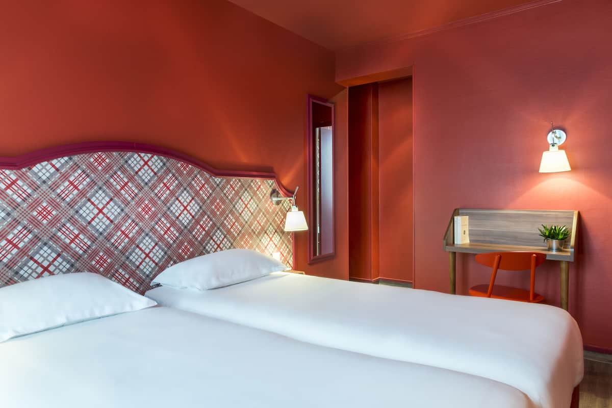 Habitación de hotel con cama, mesita de noche, lámpara y pared con diseño decorativo.