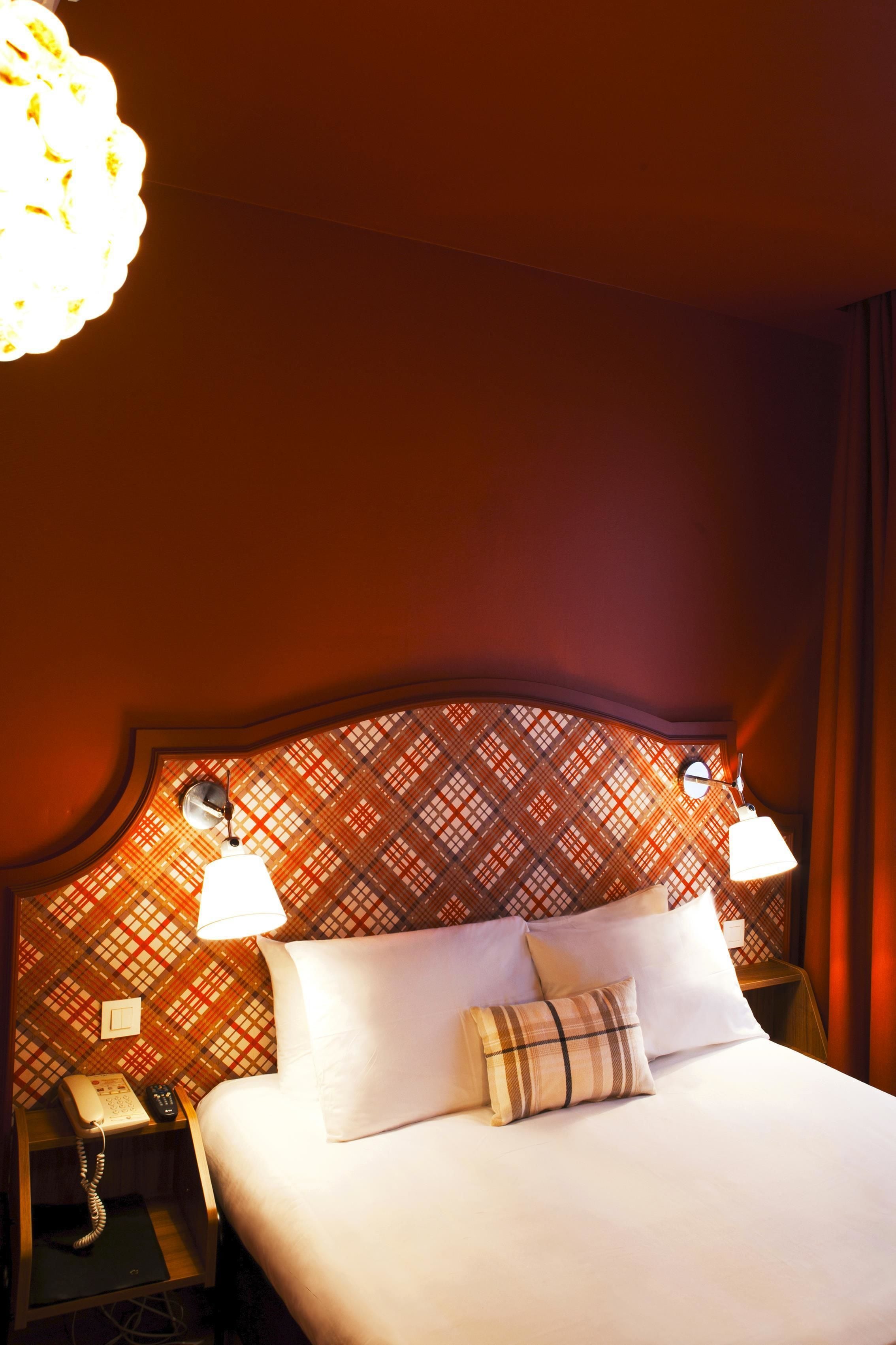 A hotel room with a large bed, two bedside lamps, a telephone, and a patterned headboard.