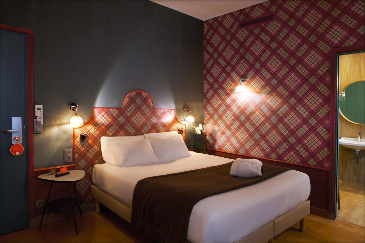 Habitación de hotel con cama, mesita de noche y baño con lavabo.
