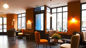 Vestíbulo de hotel con una decoración moderna, que ofrece diversas opciones de asiento y grandes ventanales con vistas a la calle.