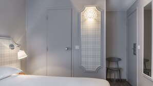 Una habitación de hotel con una cama, una lámpara de noche, una puerta con panel decorativo, una mesita y una silla.
