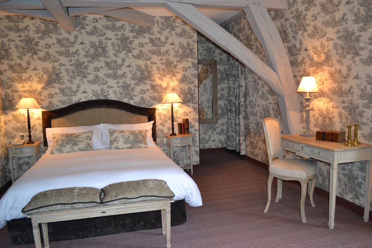 Ein Schlafzimmer mit einem großen Bett, zwei Nachttischen mit Lampen, einem Sessel und einem Schreibtisch mit Spiegel.