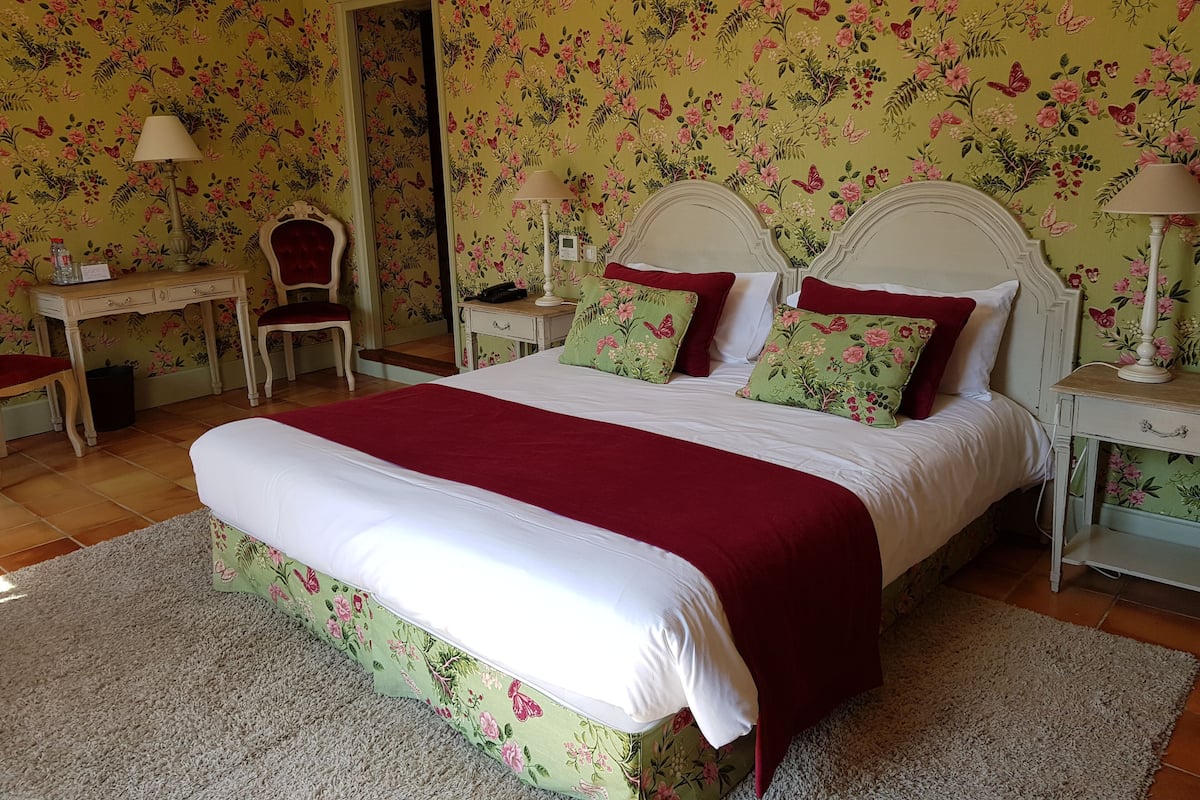 Ein Schlafzimmer mit einem großen Bett, Blumenwallpaper, einem Schreibtisch und einem Stuhl.