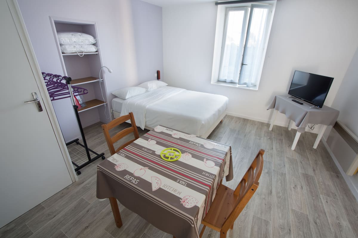 Un dormitorio con cama, televisión, armario y una mesa con mantel.