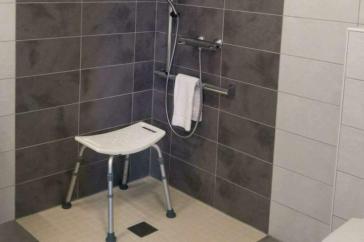 Un baño con ducha, un perchero blanco y un asiento de ducha blanco.