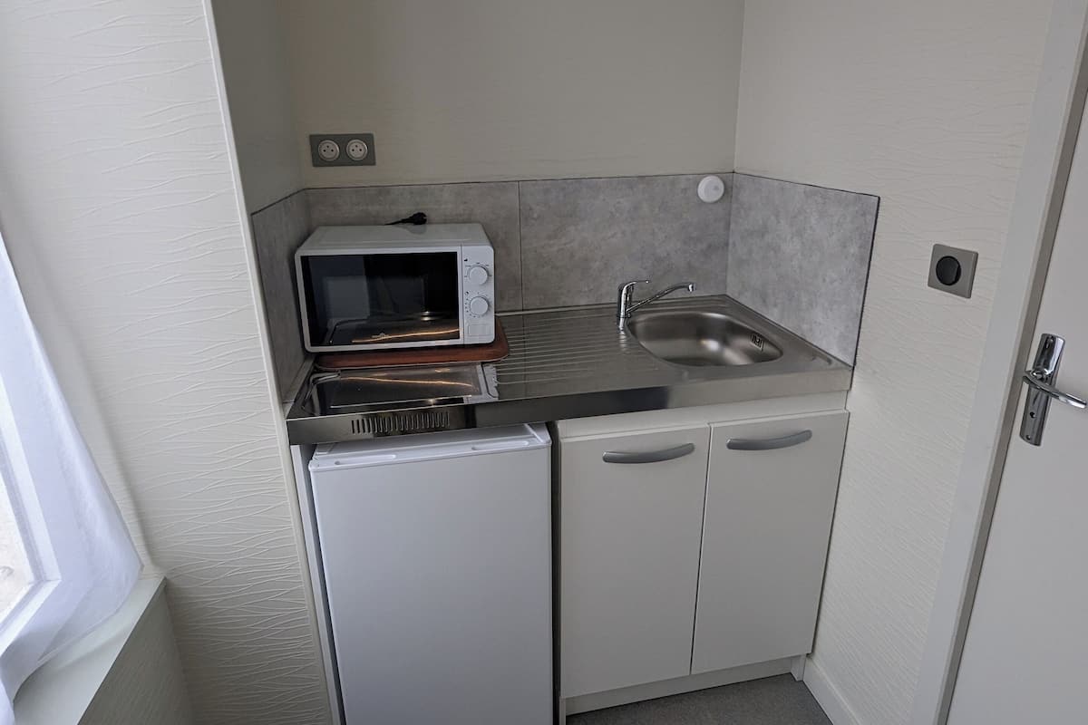 Una kitchenette compacta con microondas, refrigerador pequeño, pileta y ventana.