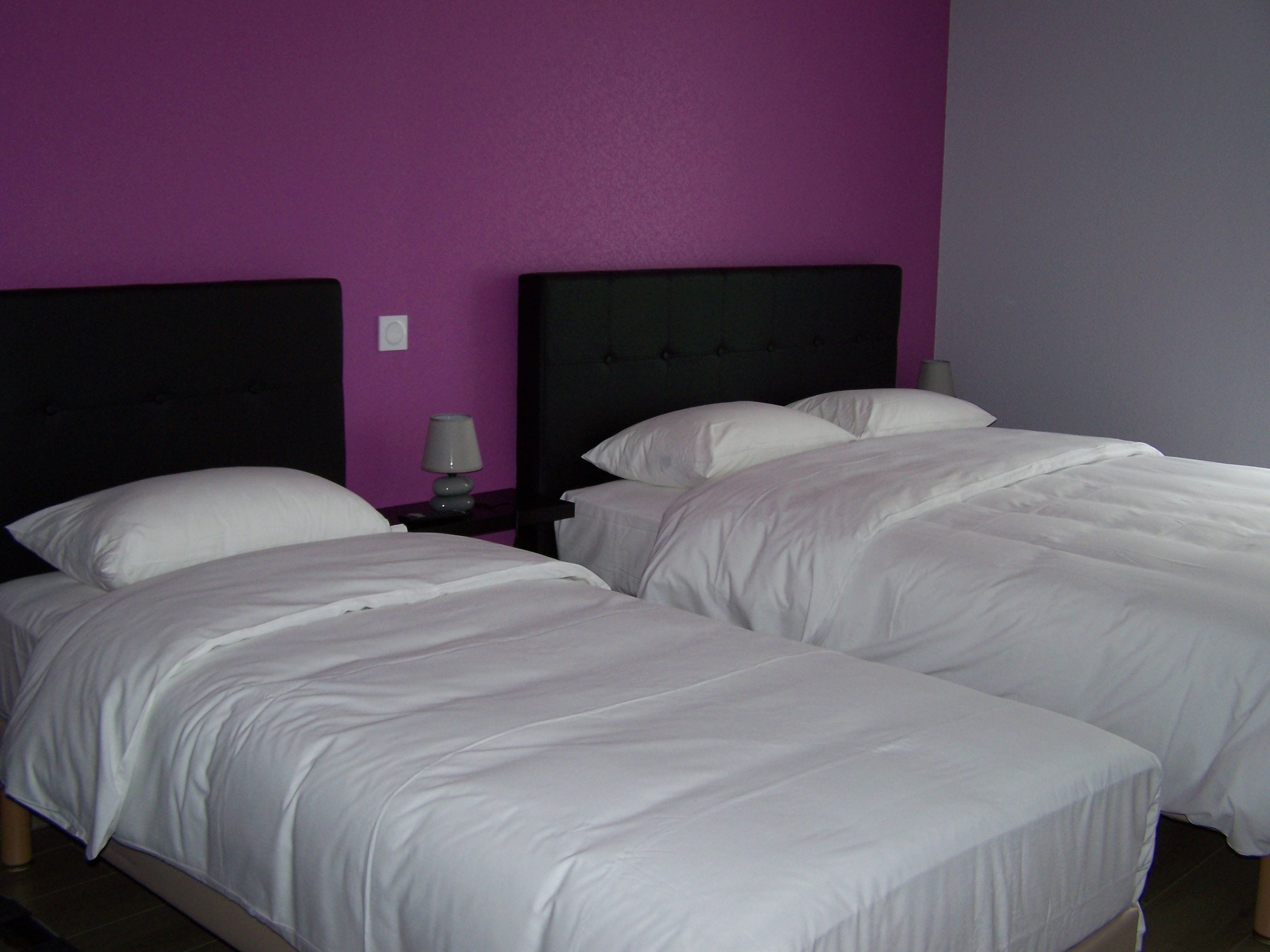 Ein Hotelzimmer mit zwei Betten, einem Nachttisch mit Lampe und einer violetten Wand.