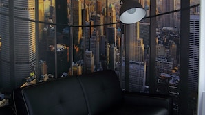 Una habitación moderna con un sofá de cuero negro, una cama blanca y un mural con vistas a la ciudad.