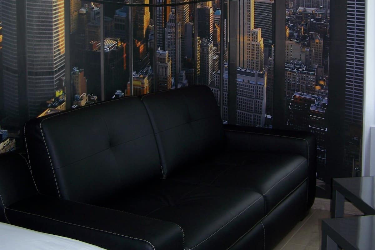 Una habitación moderna con un sofá de cuero negro, una cama blanca y un mural con vistas a la ciudad.