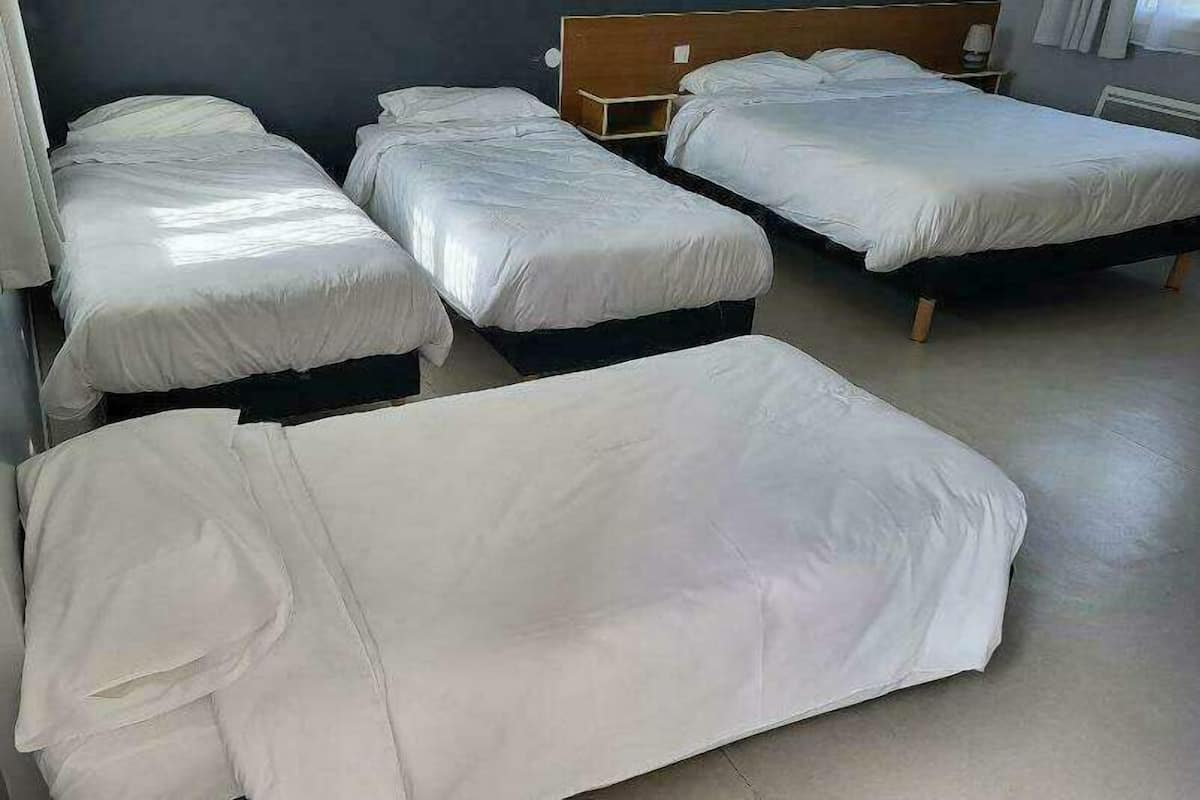 Una habitación con cuatro camas individuales, cada una con cabecero de madera y ropa de cama blanca.