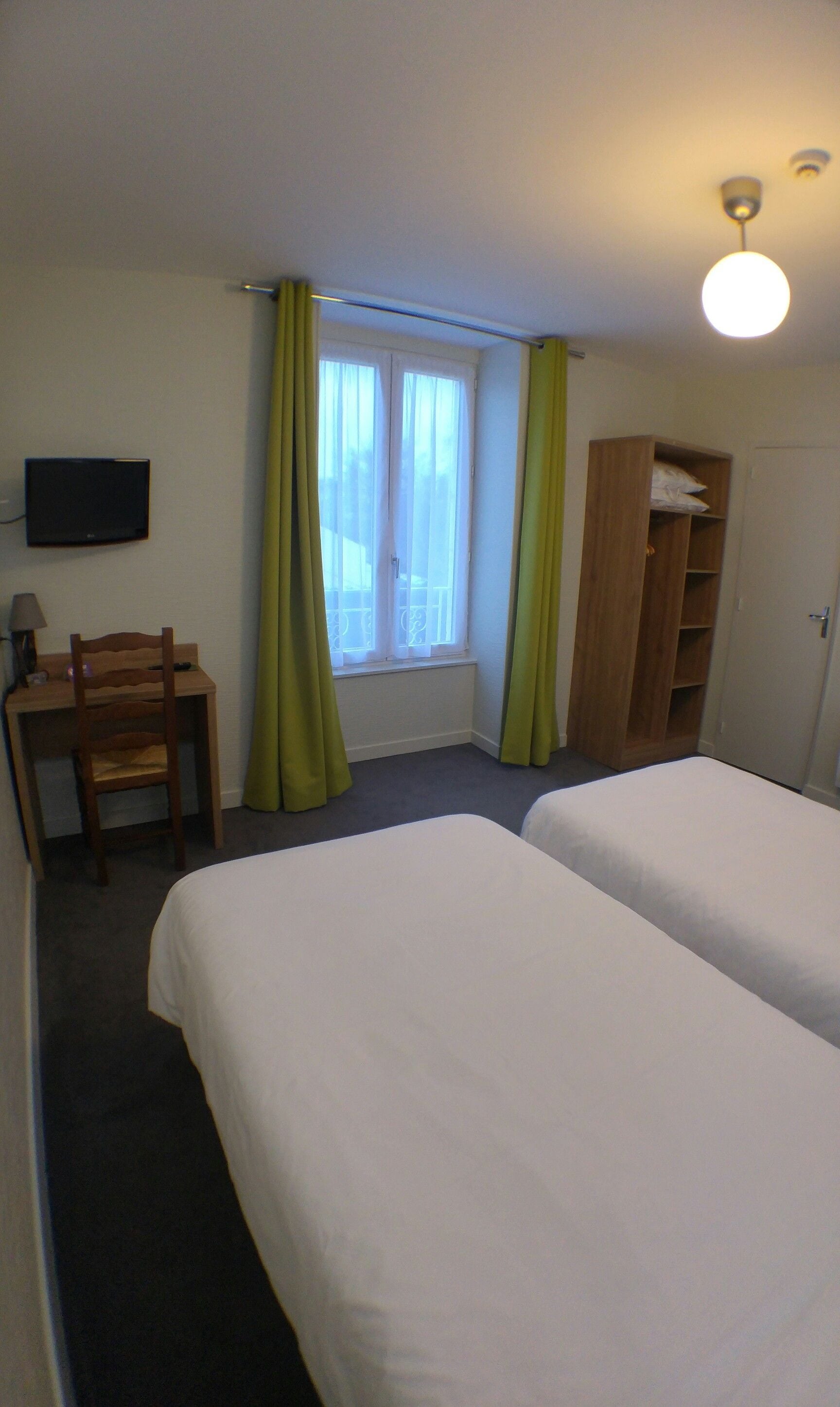 A hotel room with two beds, a desk with a chair, a TV mounted on the wall, and a window with curtains.