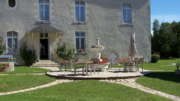 Un edificio de piedra grande con un patio jardín, mobiliario exterior y una fuente.