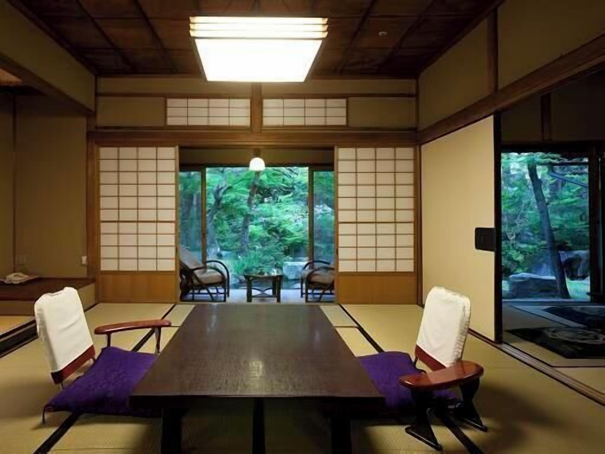 Una habitación japonesa tradicional con suelo de tatami, una mesita baja y puertas correderas que dan a vistas de follaje verde.