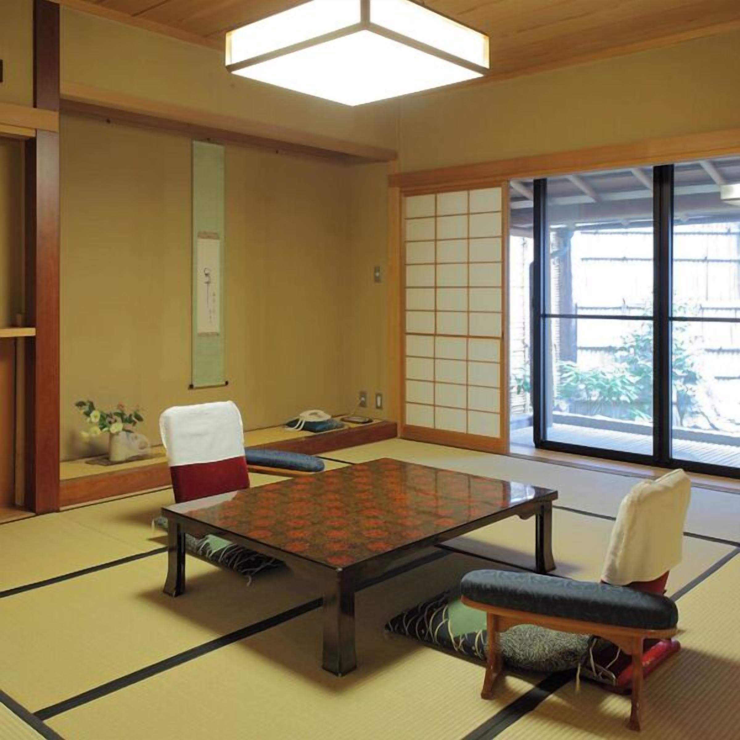 Una habitación con esteras de tatami, una mesa baja, sillas y puertas correderas.