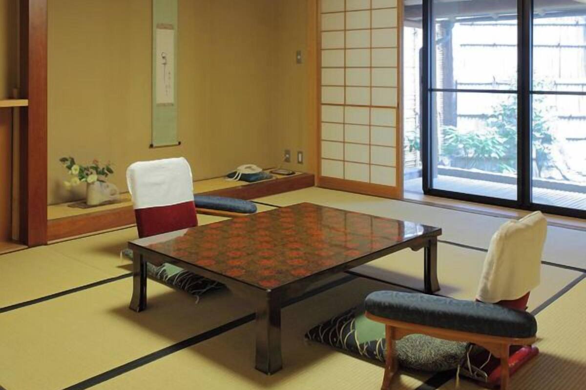 A tatami mat room with a low table, chairs, and sliding doors.
