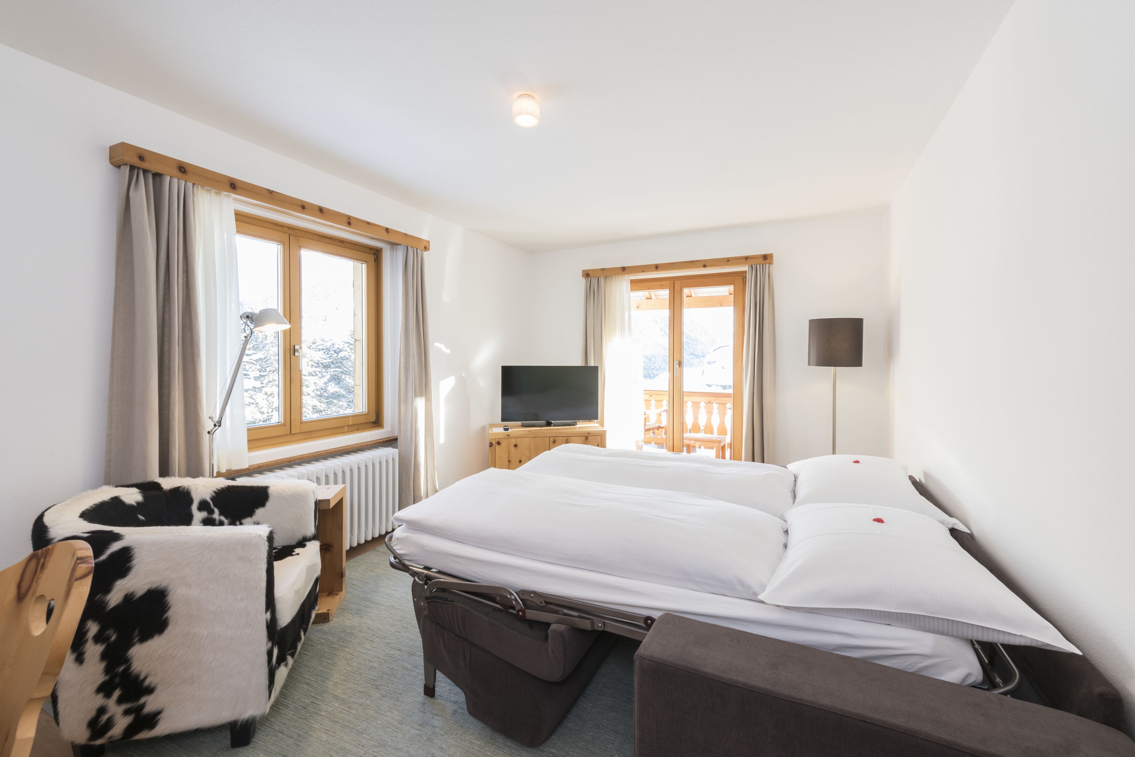 Una habitación de hotel con una cama grande, un televisor, una silla y una ventana con cortinas.