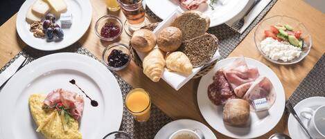 Una mesa de desayuno con diversos platos, incluyendo huevos, tocino, queso, cruasanes y frutas.