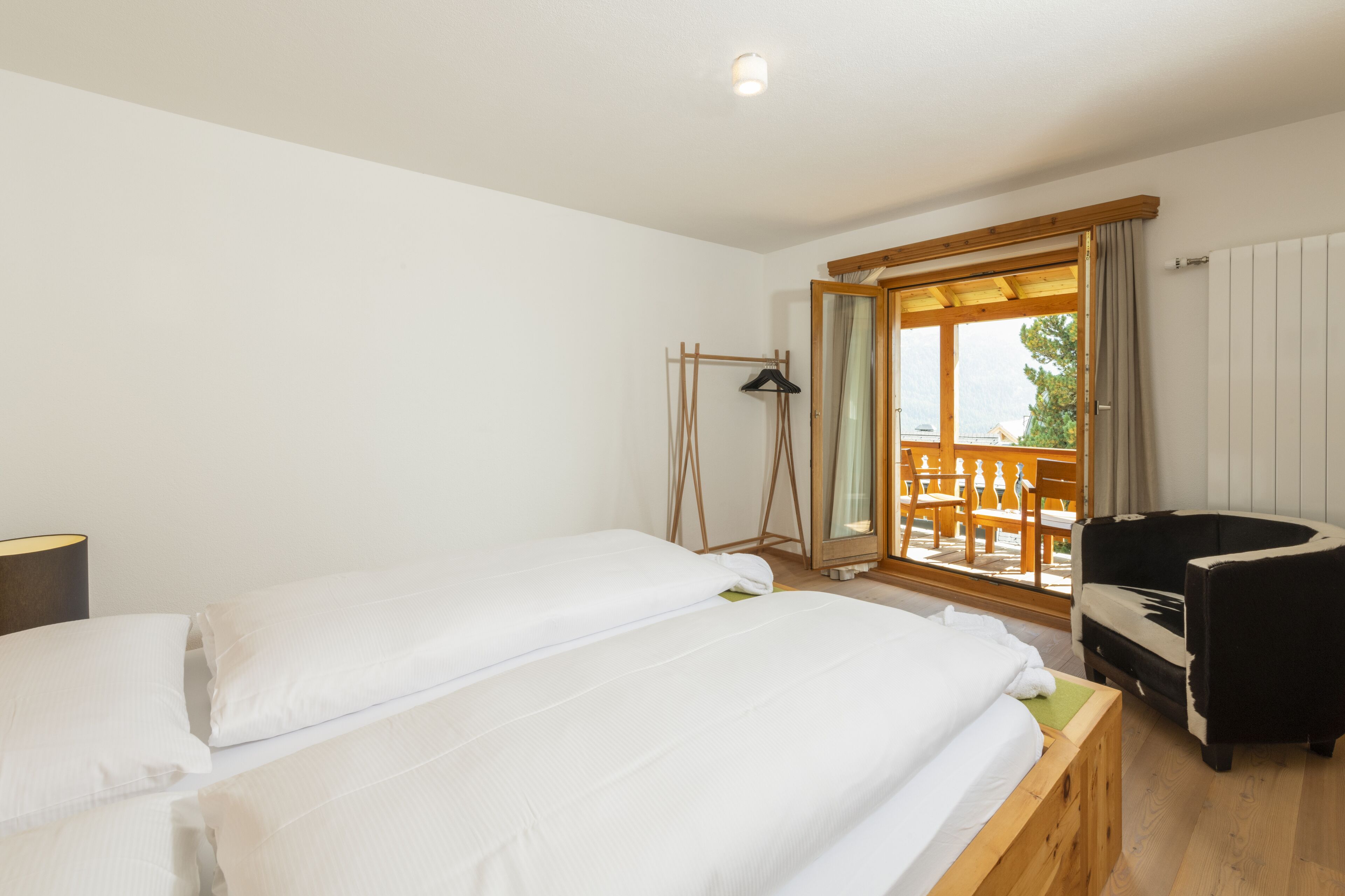 Una camera da letto con due letti, una panca in legno, una sedia bianco e nero e una finestra con vista su una terrazza esterna.