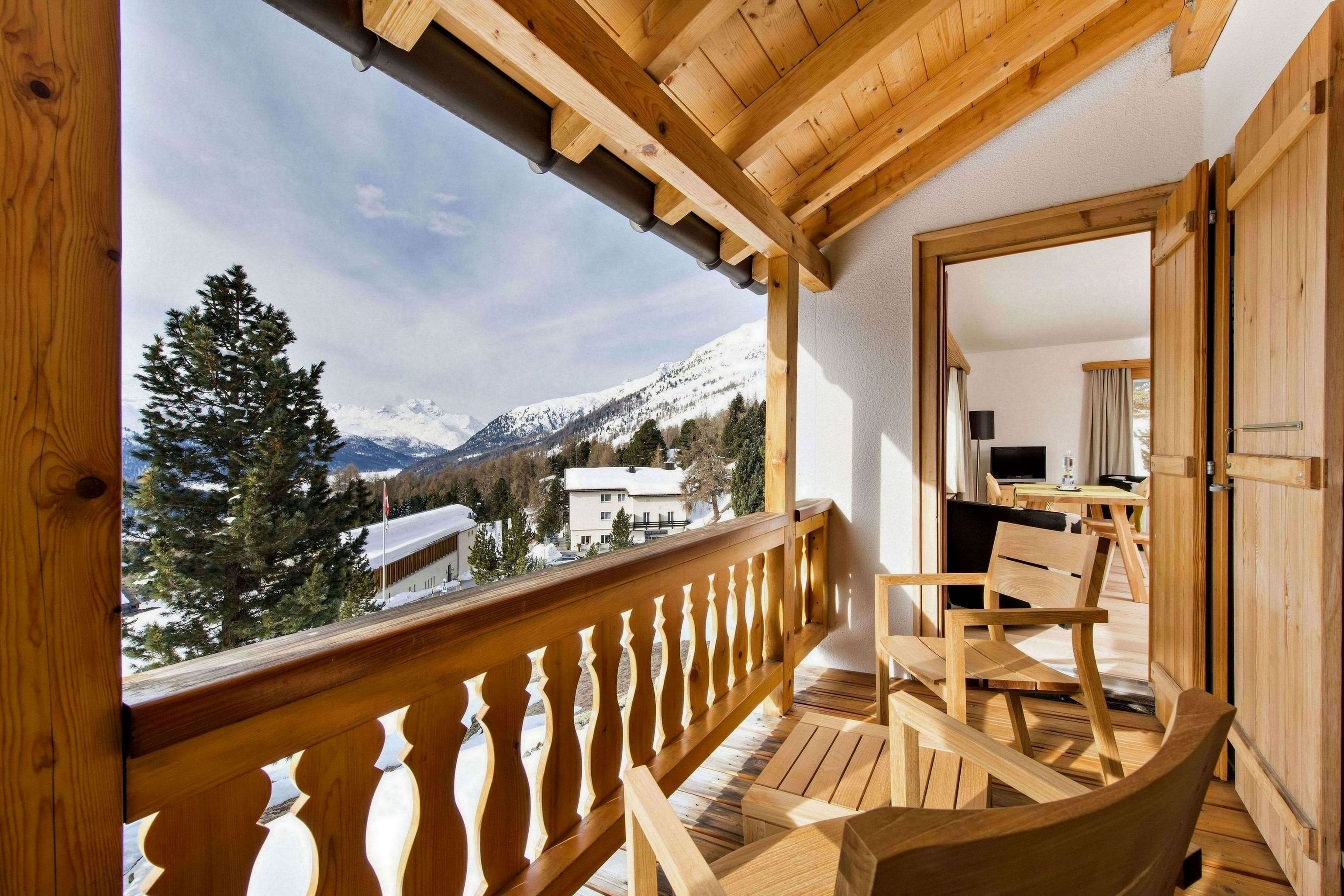 A wooden balcony with a view of snow-capped mountains and a pine tree.