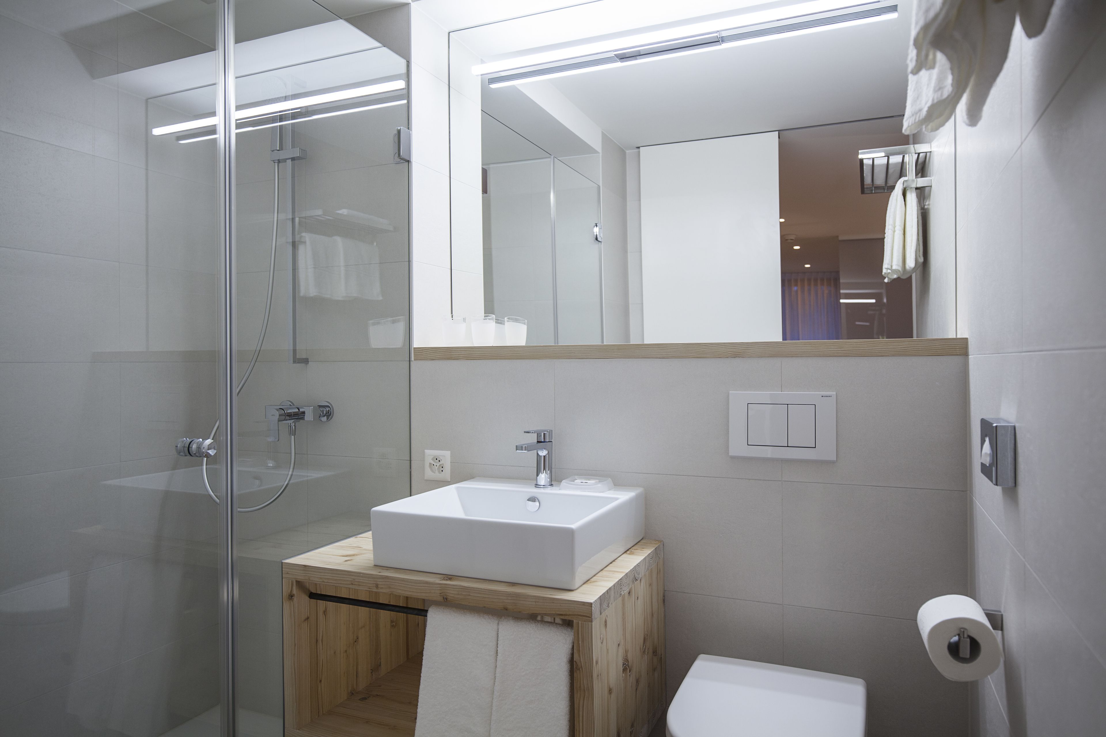 A modern bathroom with a glass-enclosed shower, a wooden vanity with a white sink, and a large mirror.