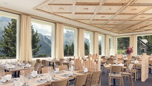 A restaurant with multiple tables set for dining, large windows offering mountain views, and a wooden ceiling. - Berghotel Randolins (St. Moritz)