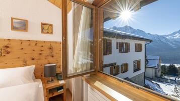 A bedroom with a wooden headboard, a bedside table with a lamp, and a window with a view of snow-covered mountains.