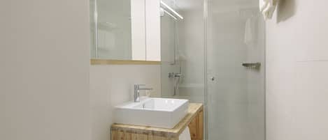 A modern bathroom with a glass shower enclosure, a wooden vanity, and a large mirror.