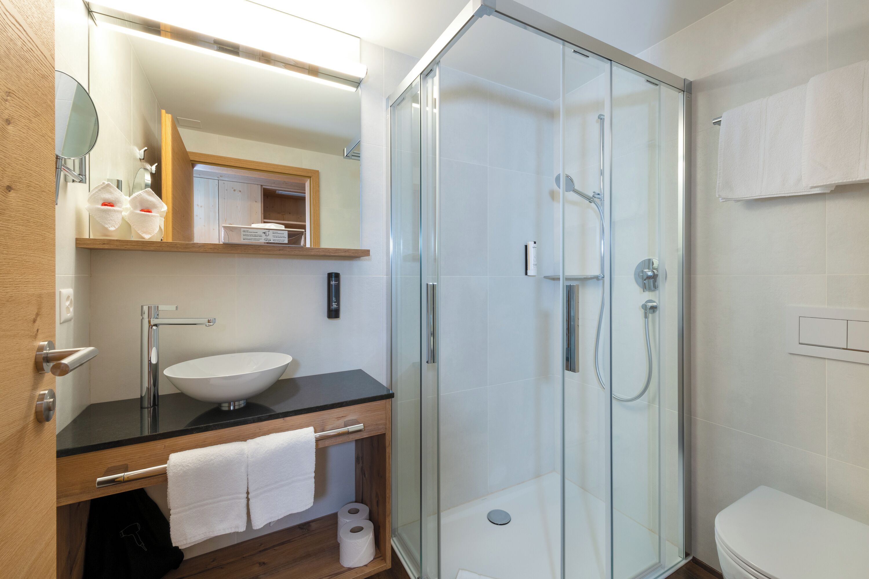 Une salle de bain moderne avec une douche à parois de verre, un lavabo blanc et un meuble-lavabo en bois.