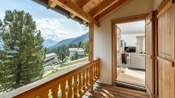 A wooden balcony with a view of mountains and a building in the background.
