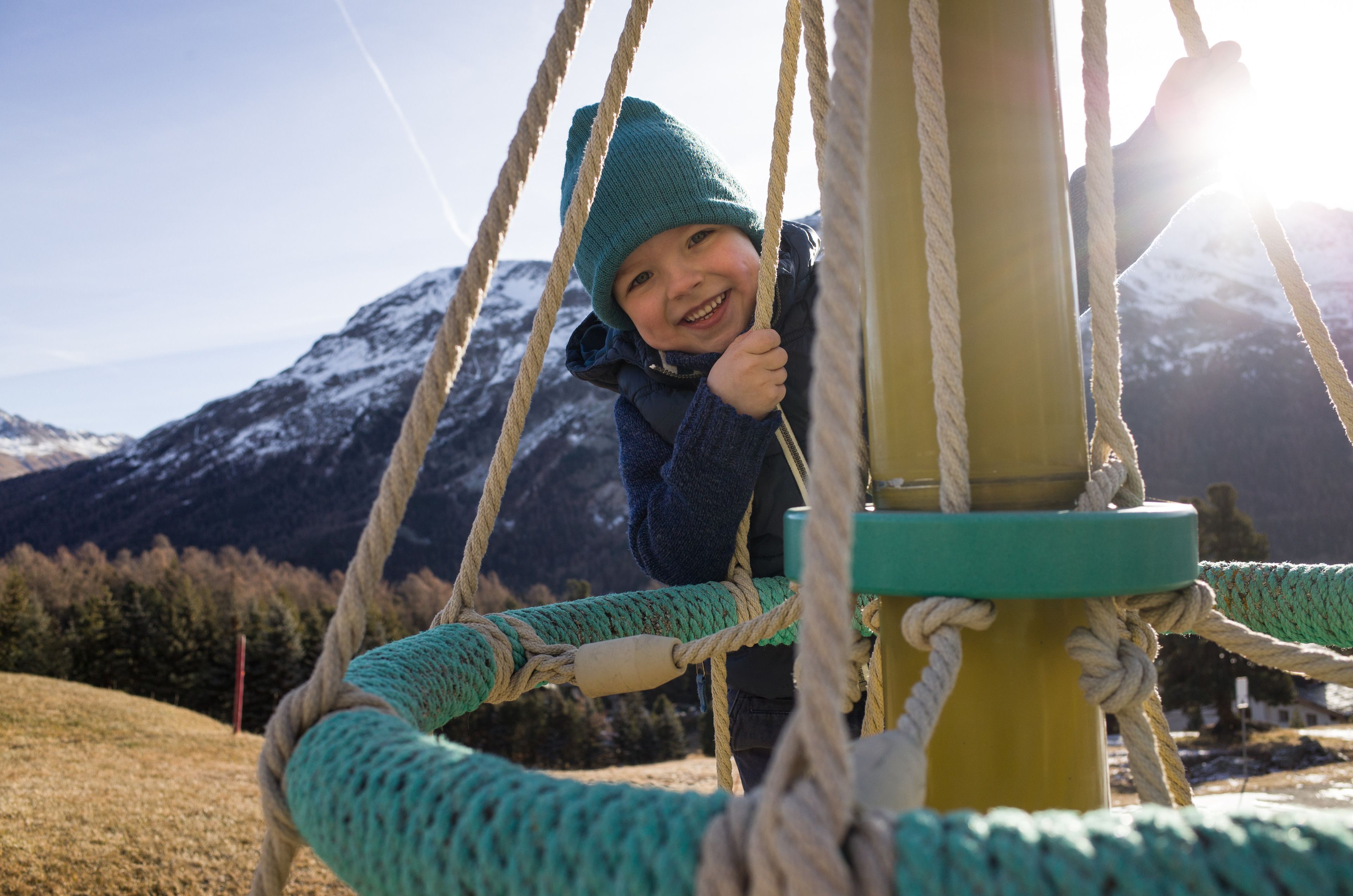 A child on a rope swing with a mountainous backdrop.