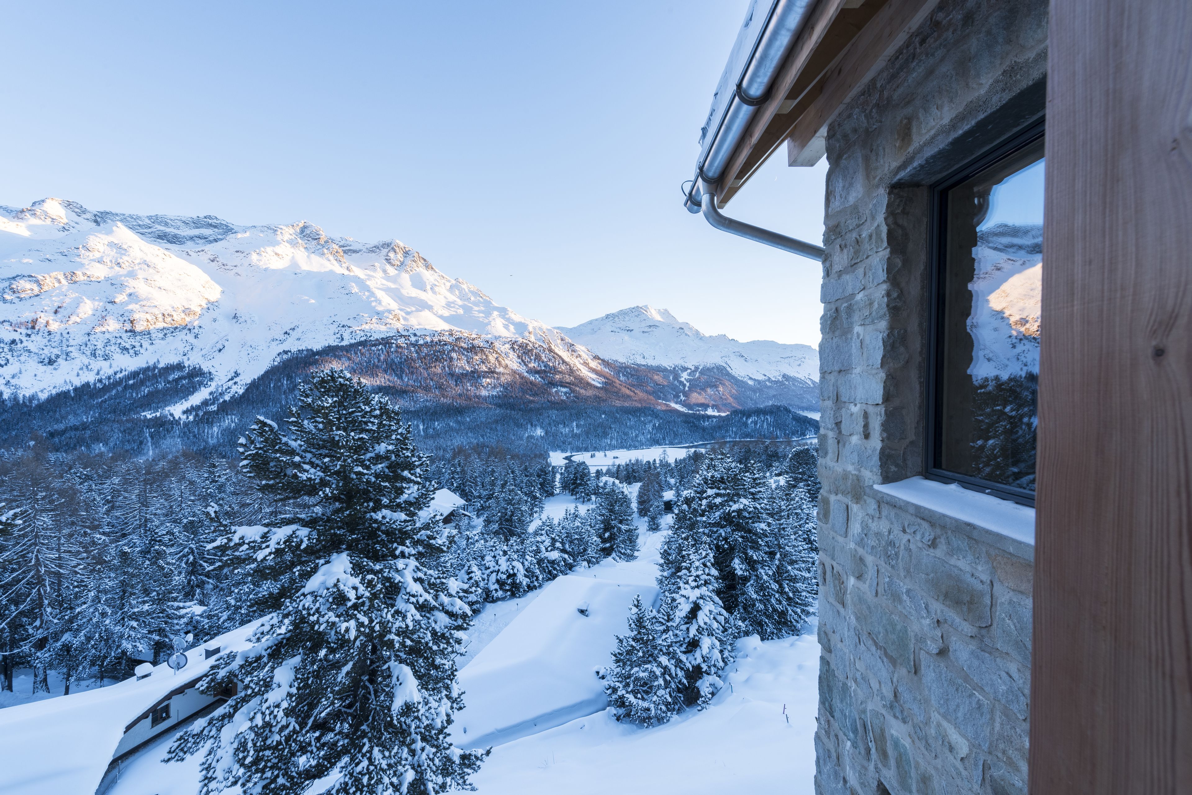 Ein Steinhäuschen mit einem Fenster mit Blick auf eine verschneite Berglandschaft.