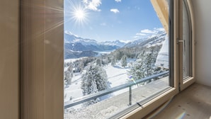 A room with a large window offering a view of snow-covered mountains and a clear sky. - Berghotel Randolins (St. Moritz)