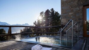 A hot tub with a wooden deck and a stone wall, overlooking a mountainous landscape. - Berghotel Randolins (St. Moritz)