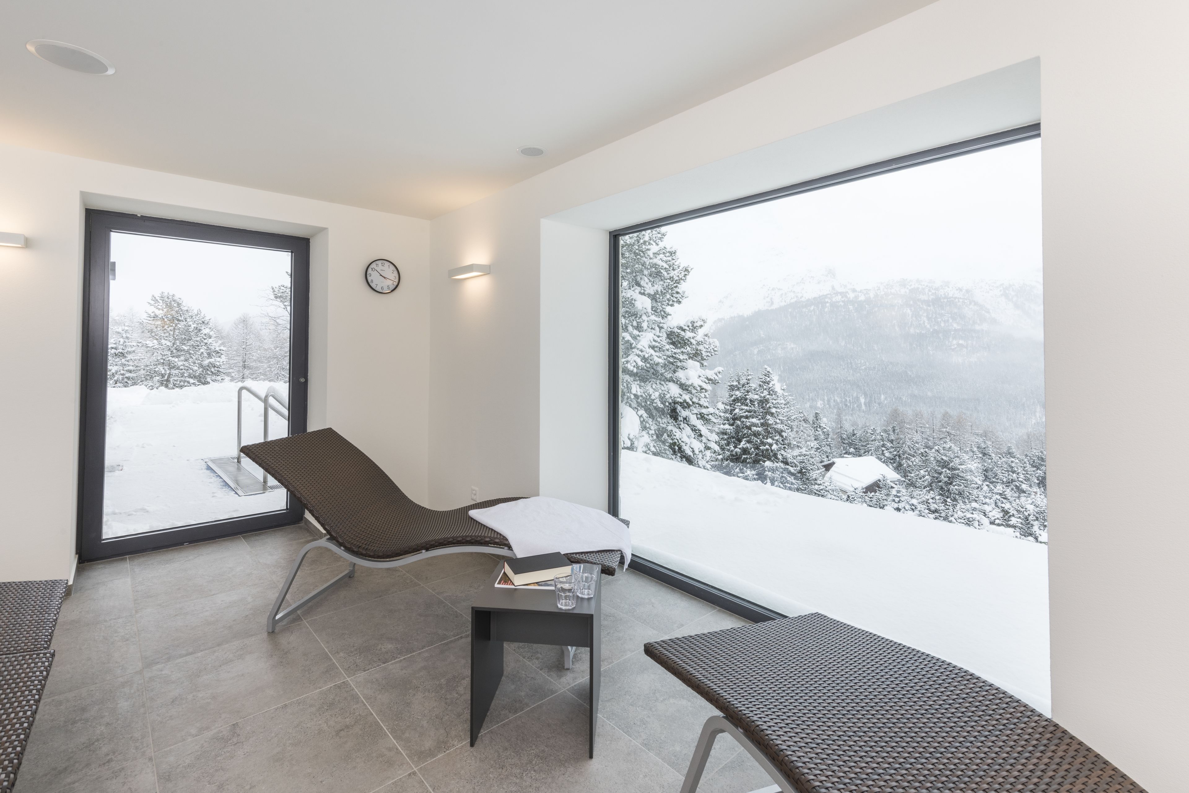 Een moderne kamer met een groot raam, een stoel, een klein tafeltje en uitzicht op een besneeuwd landschap.
