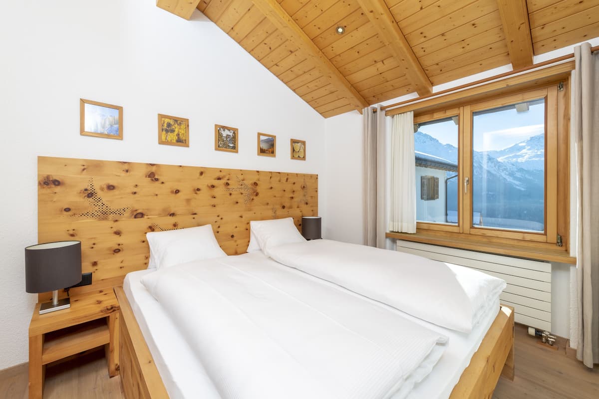 A double bed with a wooden headboard, two bedside tables with lamps, and a window with a mountain view.