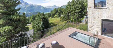 Terraza con sillas de descanso y jacuzzi con vista a un paisaje montañoso.