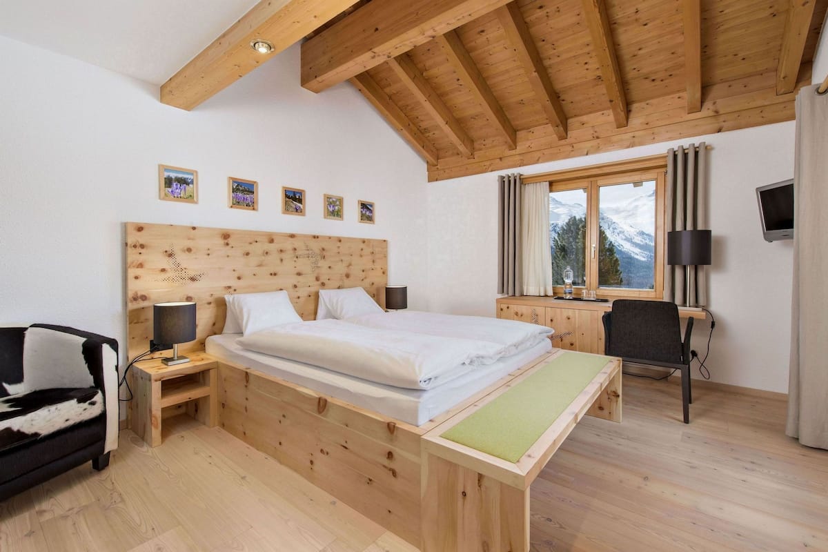 A wooden bedroom with a bed, a desk, a chair, and a TV.