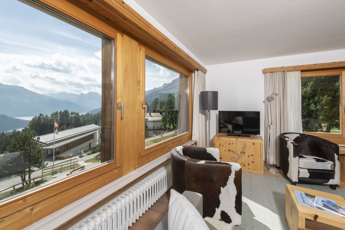 A modern room with large windows, a television, a cowhide sofa, and a wooden cabinet.