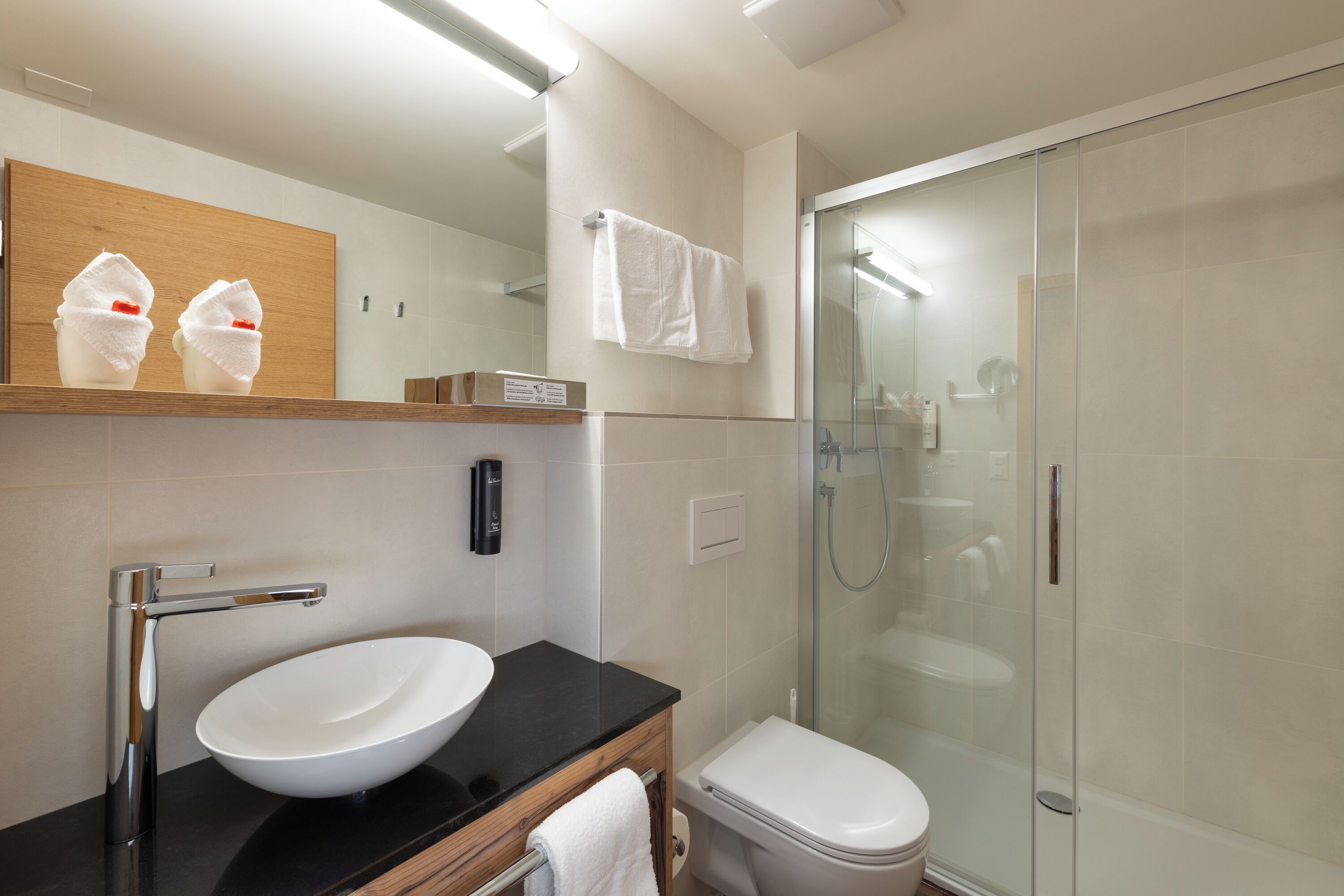 A modern bathroom with a white sink, black countertop, and a glass-enclosed shower.