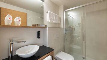 A modern bathroom with a white sink, black countertop, and a glass-enclosed shower.