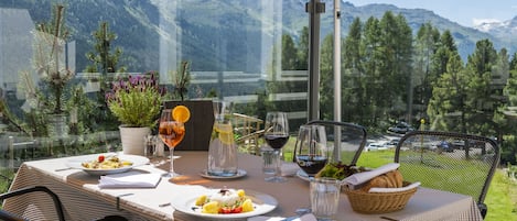 A table set for dining with a mountain view, outdoor seating, and a glass enclosure.