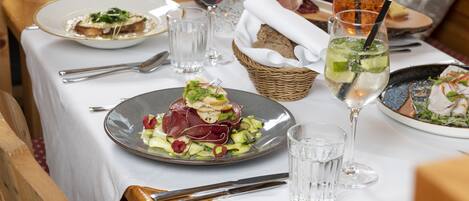 A dining table set with plates of food, glasses of water, and a basket of bread.