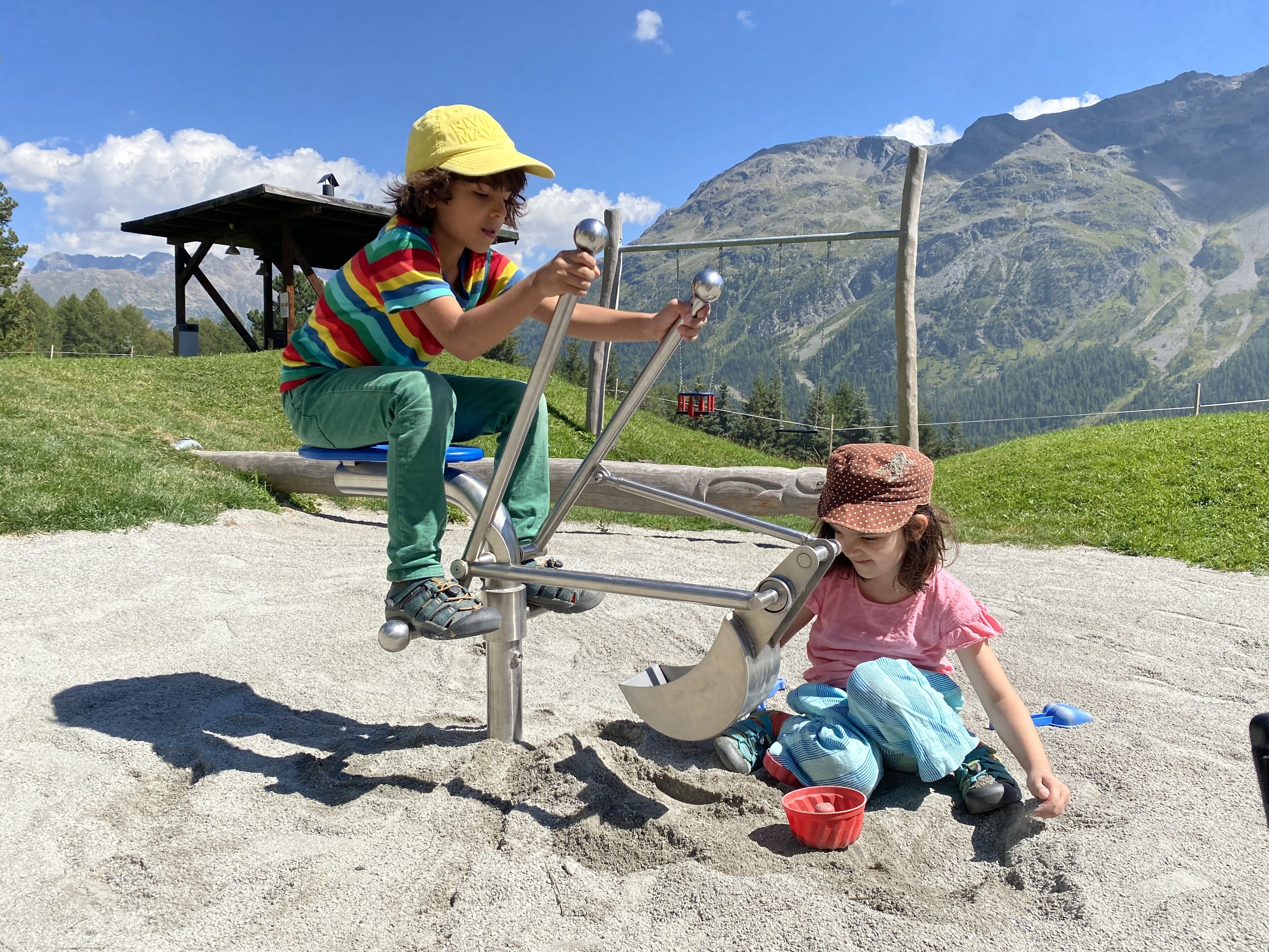 Two children playing on a seesaw in a mountainous area with a clear sky.