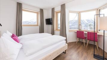 Ein Hotelzimmer mit einem hölzernen Bett, einem Schreibtisch mit Stuhl, einem Fernseher und großen Fenstern mit Blick auf die Berge.