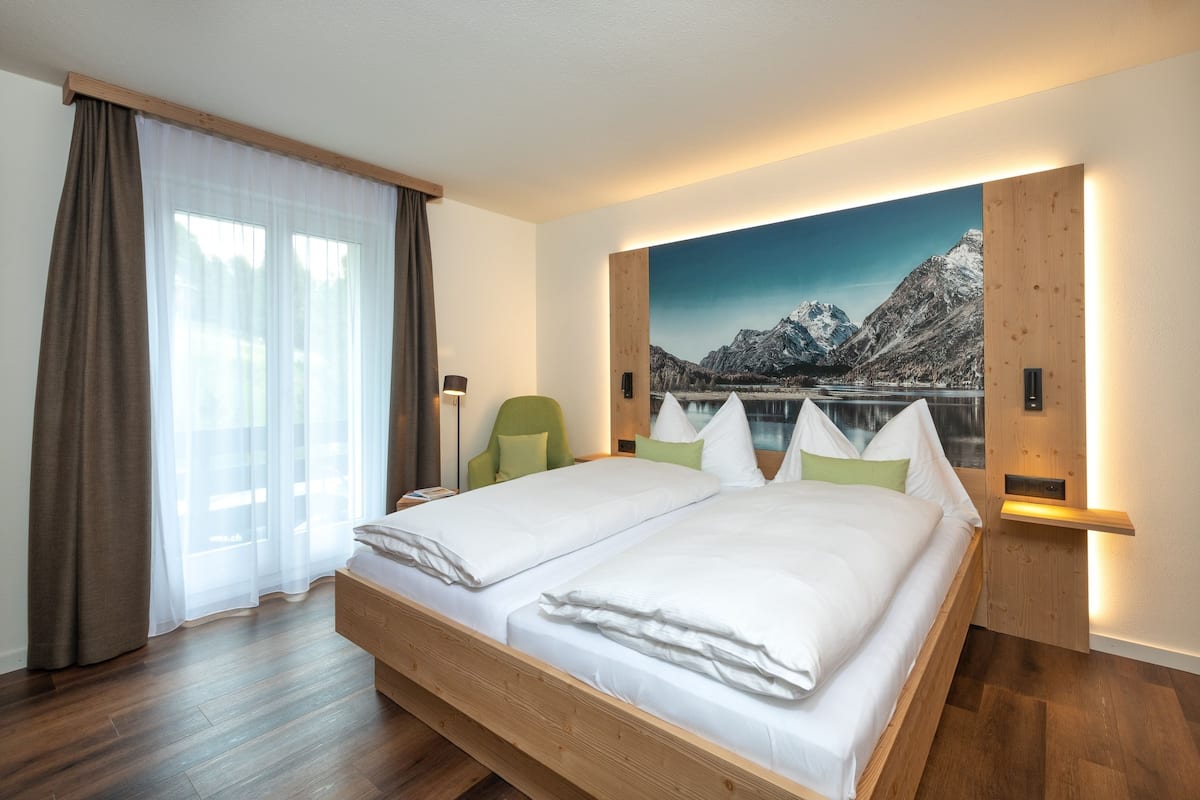 A modern hotel room with a large bed, a view of mountains, and a wooden headboard.