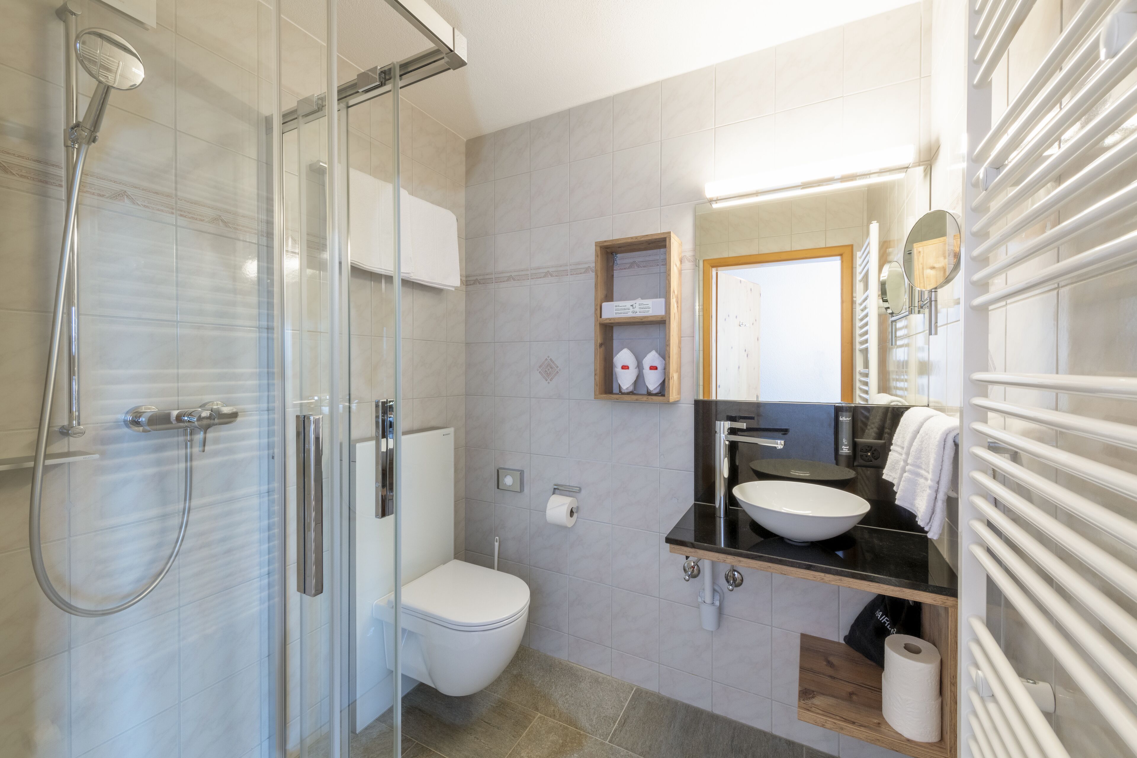 A modern bathroom with a glass-enclosed shower, a white toilet, a black sink, and a mirror above it.
