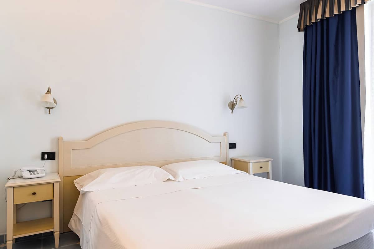 Une chambre d’hôtel avec un lit simple, des tables de chevet, une lampe et une fenêtre avec des rideaux.
