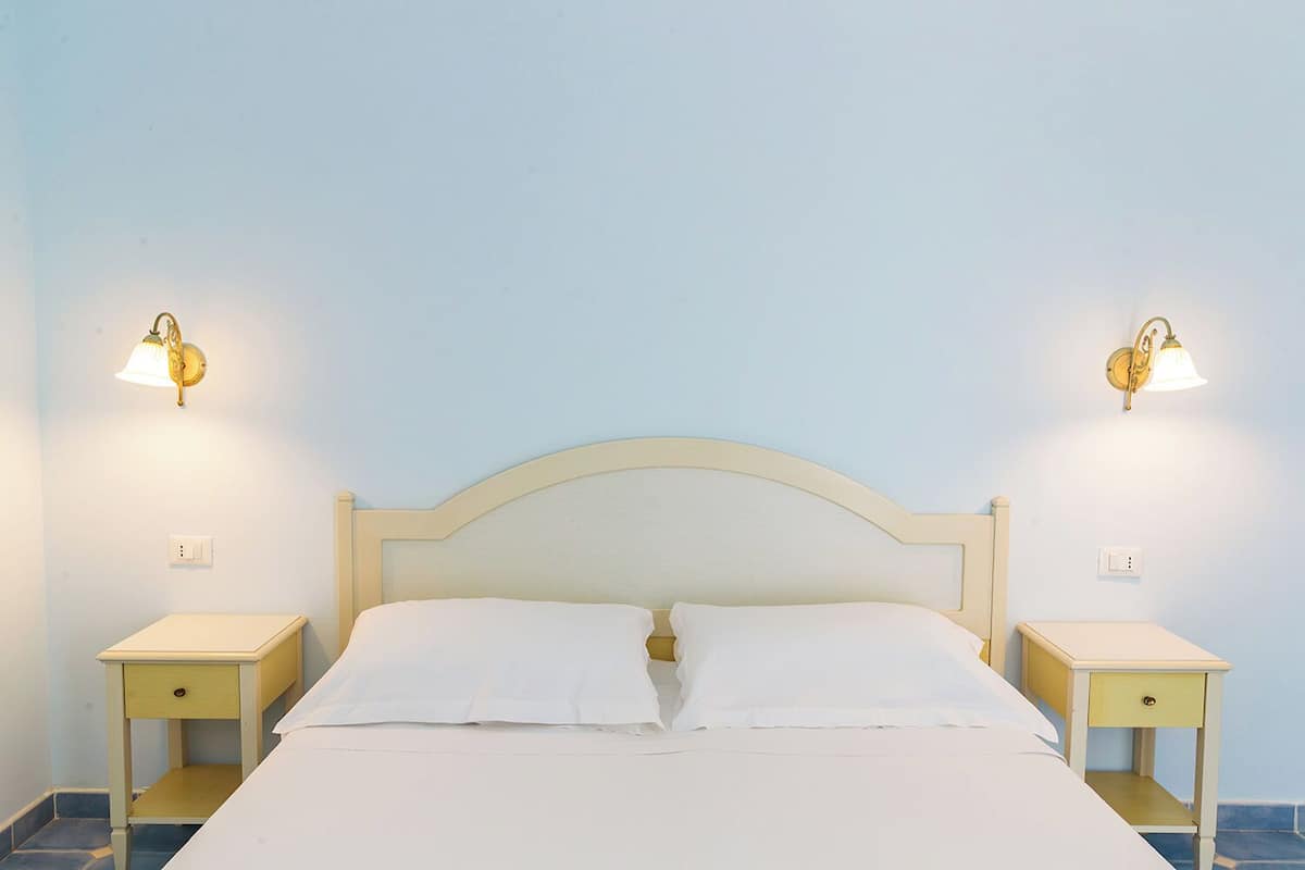 Un lit avec du linge de lit blanc, deux tables de chevet et des lampes fixées au mur.