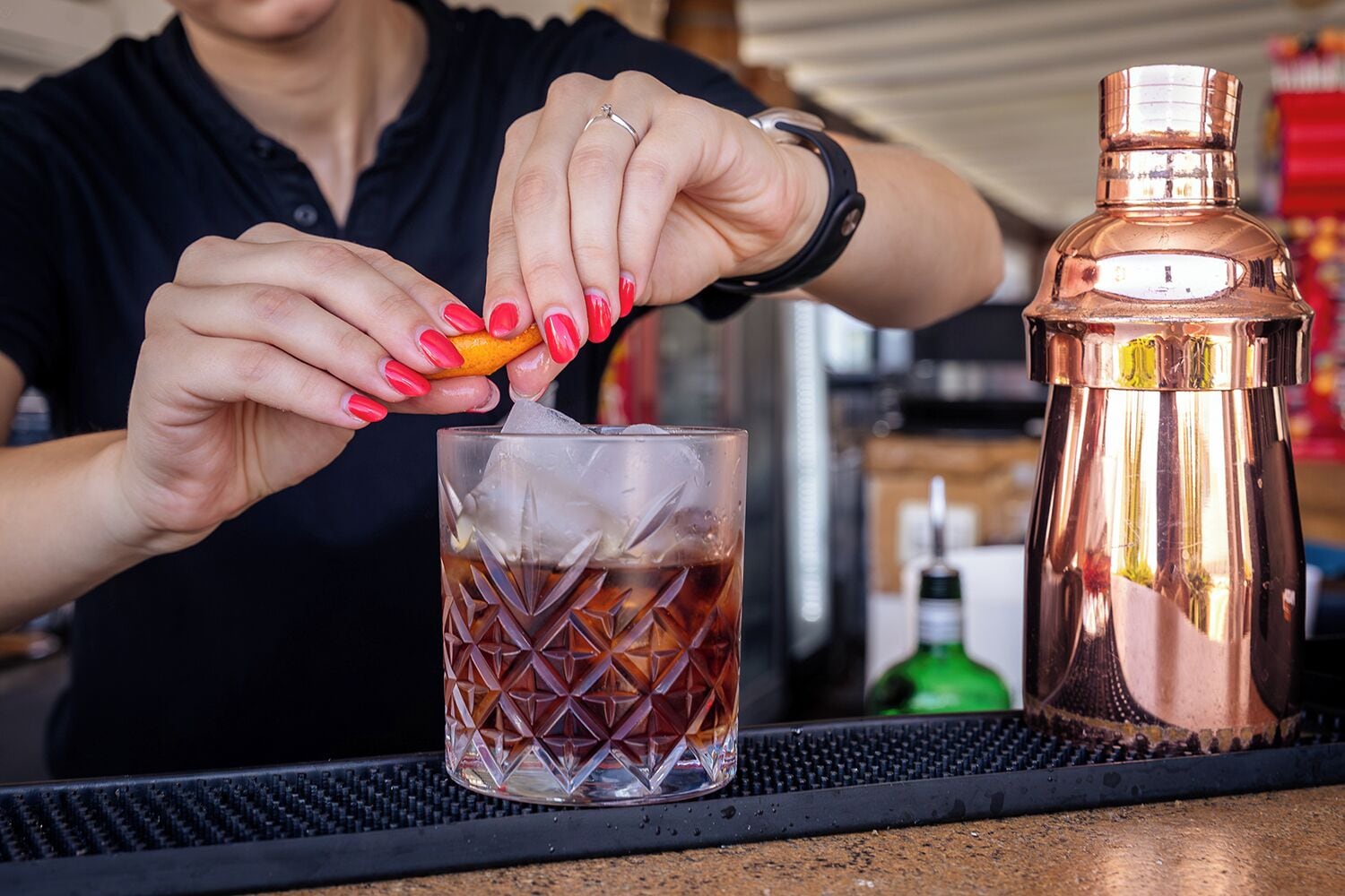 A person pouring a drink into a glass with a copper shaker on the counter.